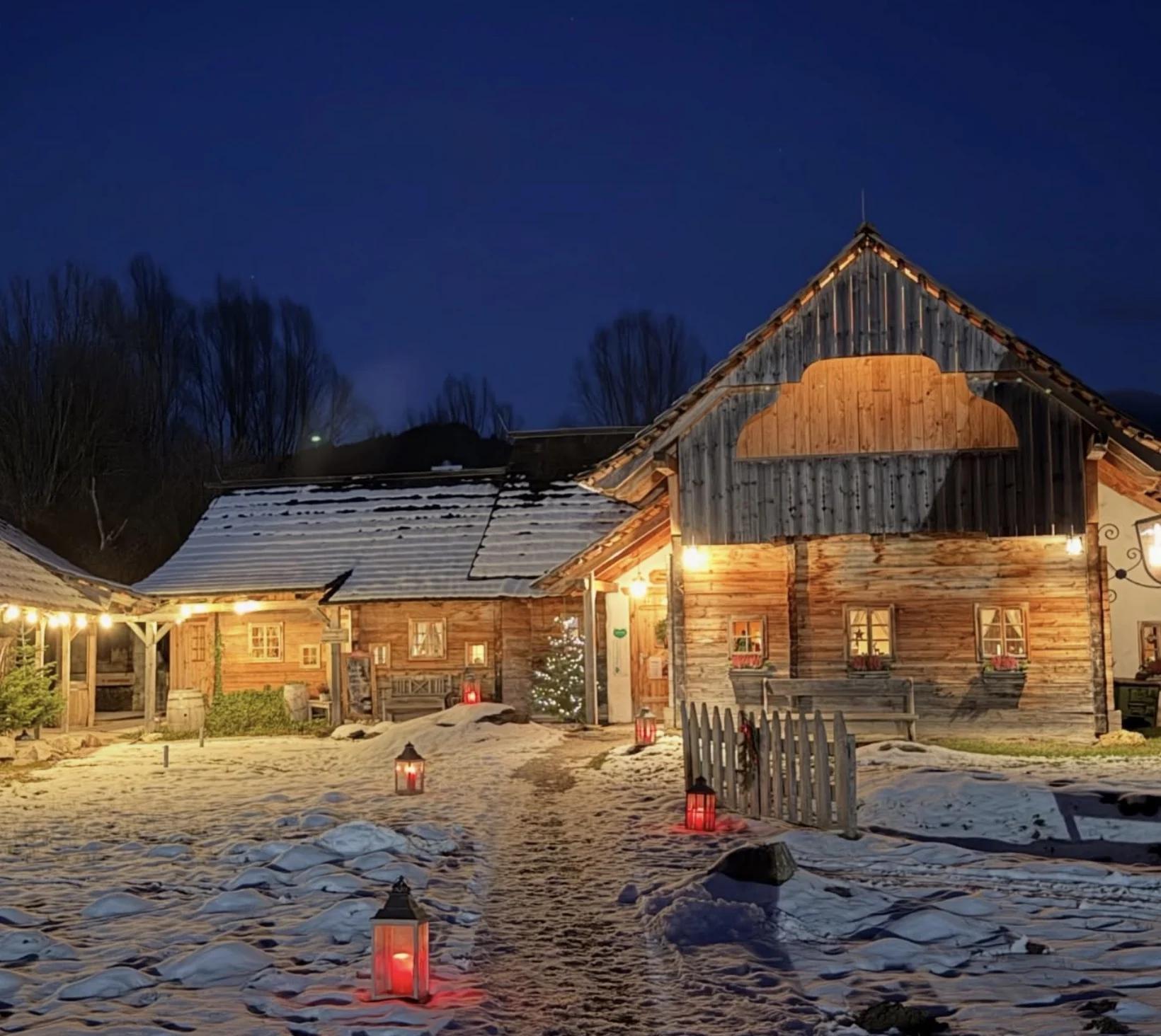 Verschneites Dörfl mit warm beleuchteten Holzhäusern und Laternen